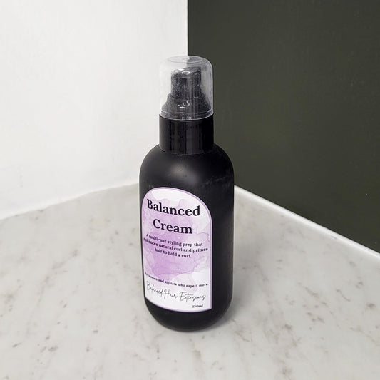 Black bottle of 'Balanced Cream' on a marble surface with a neutral background